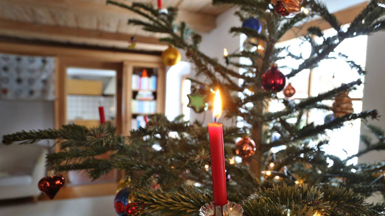 Eine Kerze brennt an einem geschmückten Weihnachtsbaum.