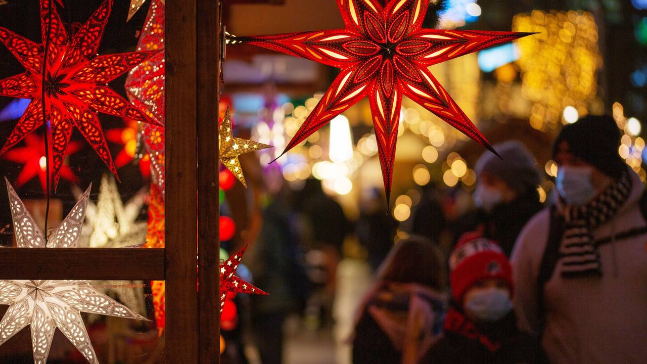 Eine Familie geht mit Mund-Nasen-Schutz auf einem Weihnachtsmarkt an einem Marktstand mit leuchtenden Sternen vorbei.