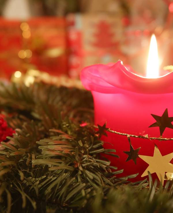 Eine Adventskerze brennt am 24.12.2013 in Hamburg, im Hintergrund liegen Weihnachtsgeschenke.