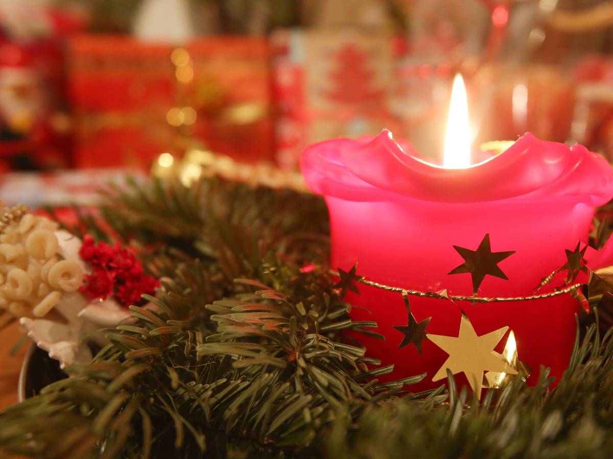 Eine Adventskerze brennt am 24.12.2013 in Hamburg, im Hintergrund liegen Weihnachtsgeschenke.