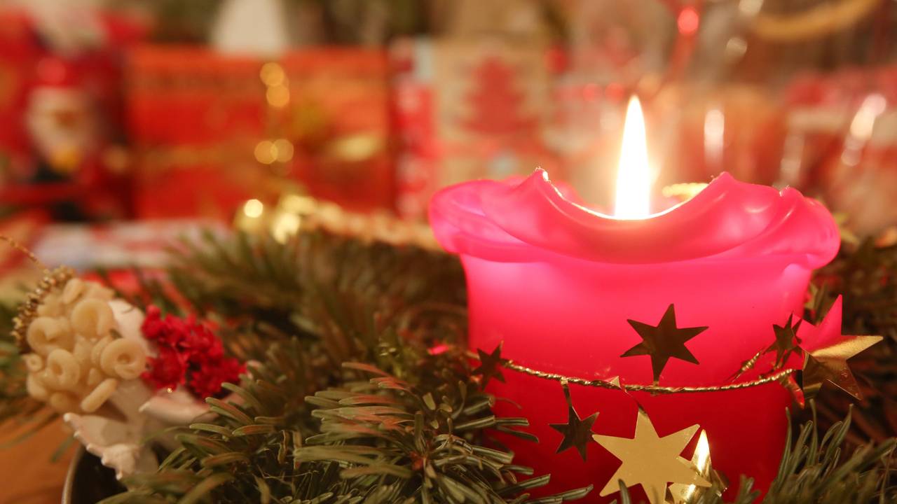 Eine Adventskerze brennt am 24.12.2013 in Hamburg, im Hintergrund liegen Weihnachtsgeschenke.