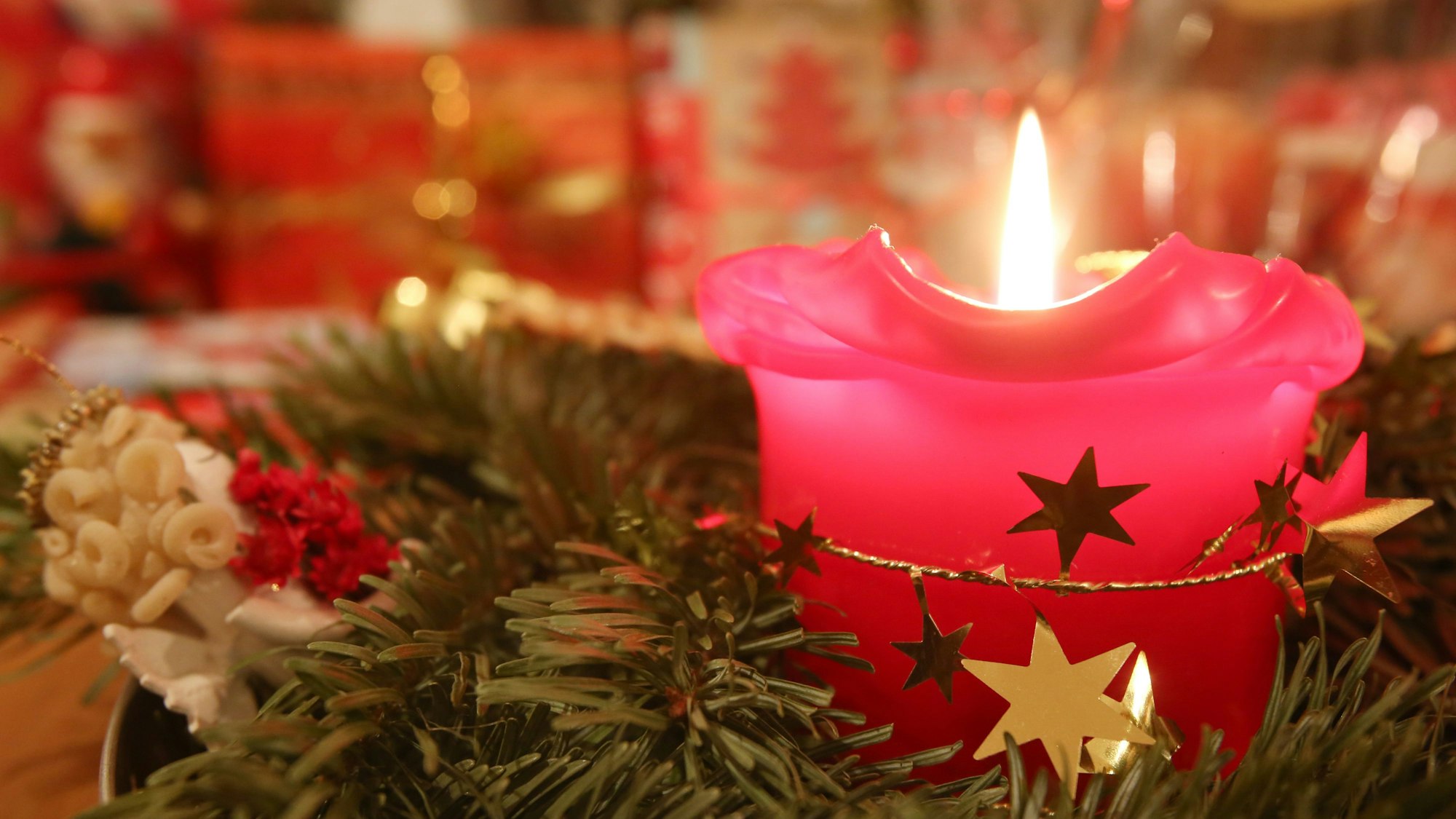 Eine Adventskerze brennt am 24.12.2013 in Hamburg, im Hintergrund liegen Weihnachtsgeschenke.