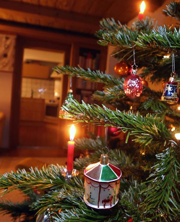 Eine ältere Frau sitzt hinter einem geschmückten Weihnachtsbaum.