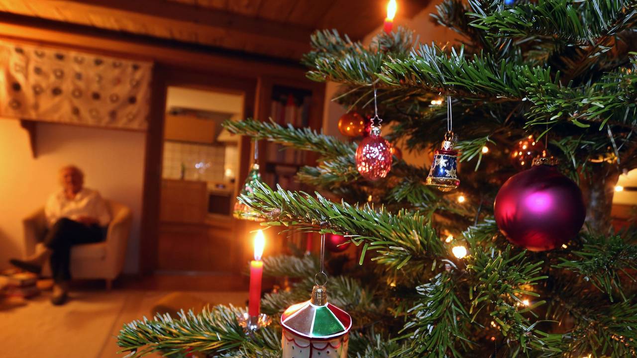 Eine ältere Frau sitzt hinter einem geschmückten Weihnachtsbaum.