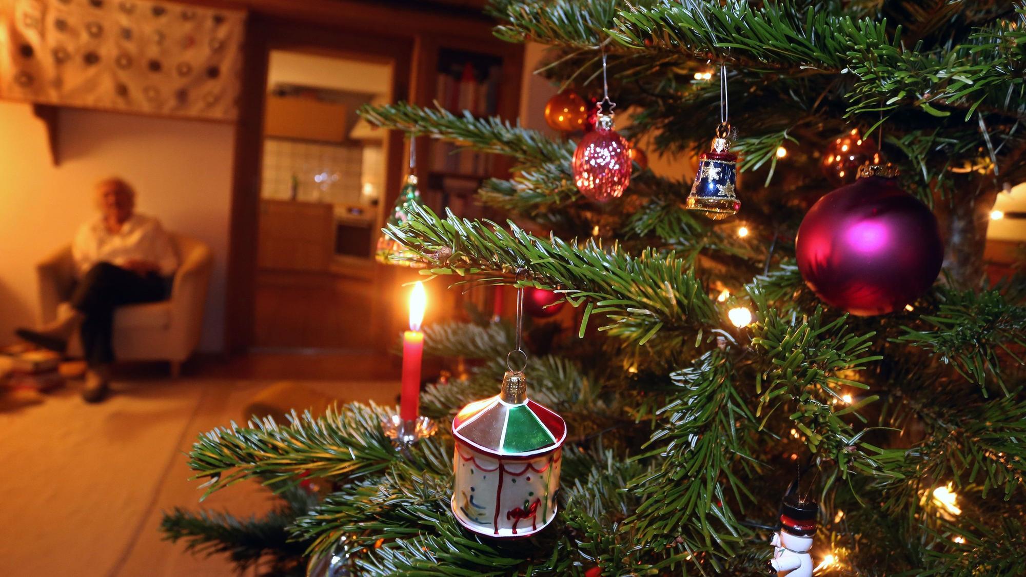 Eine ältere Frau sitzt hinter einem geschmückten Weihnachtsbaum.