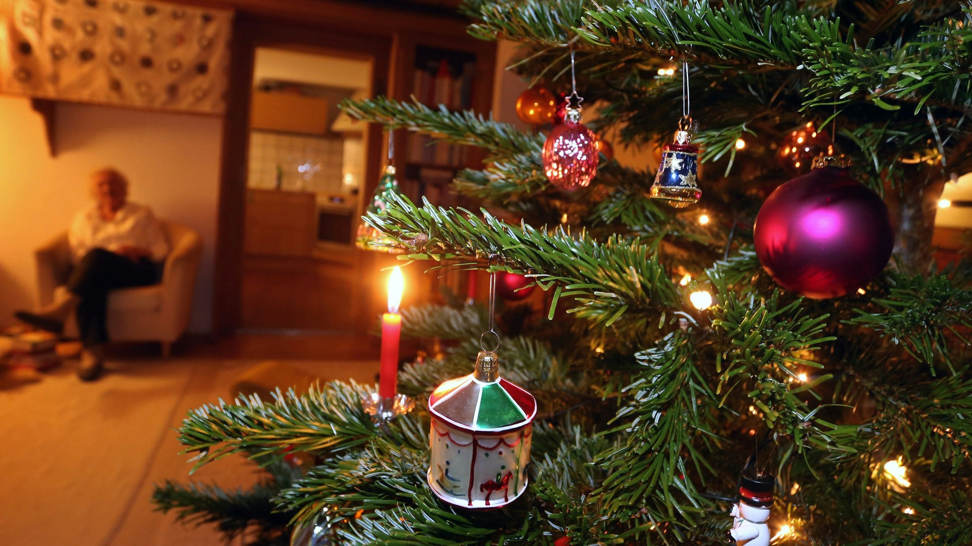Eine ältere Frau sitzt hinter einem geschmückten Weihnachtsbaum.