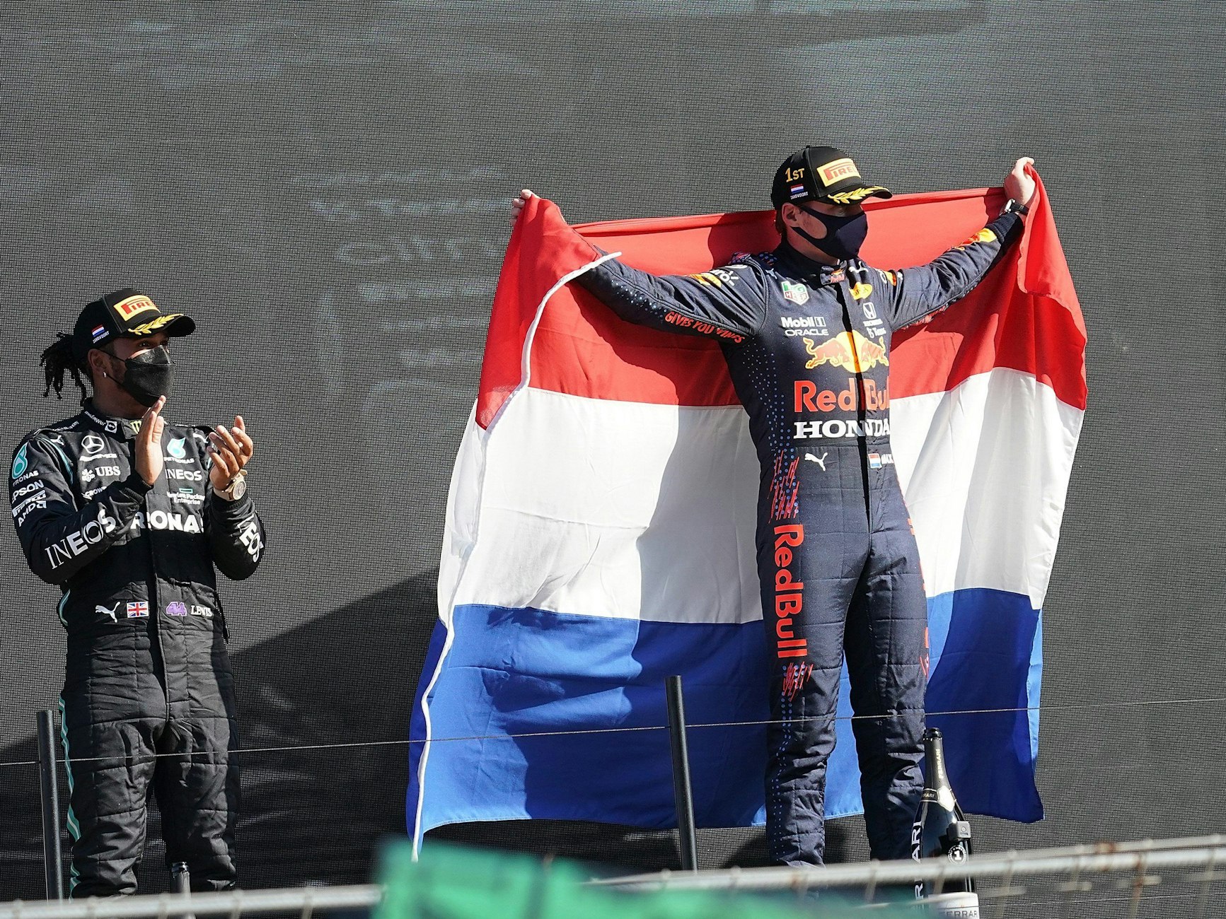 Der Zweitplatzierte Lewis Hamilton (l) aus Großbritannien vom Team Mercedes-AMG Petronas Formula One Team applaudiert während der Sieger Max Verstappen aus den Niederlanden vom Team Red Bull Racing Honda eine niederländische Fahne hält.