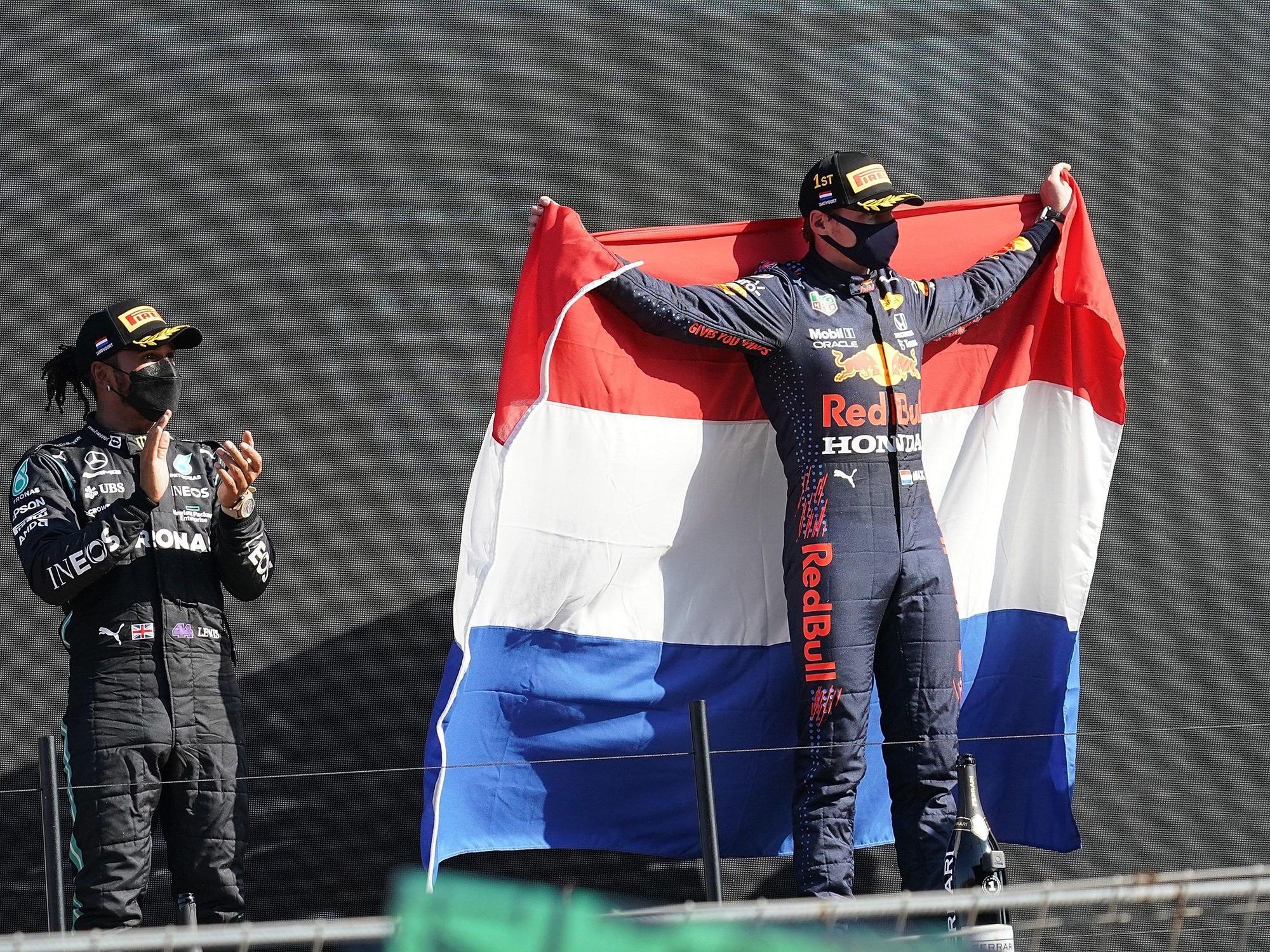 Der Zweitplatzierte Lewis Hamilton (l) aus Großbritannien vom Team Mercedes-AMG Petronas Formula One Team applaudiert während der Sieger Max Verstappen aus den Niederlanden vom Team Red Bull Racing Honda eine niederländische Fahne hält.