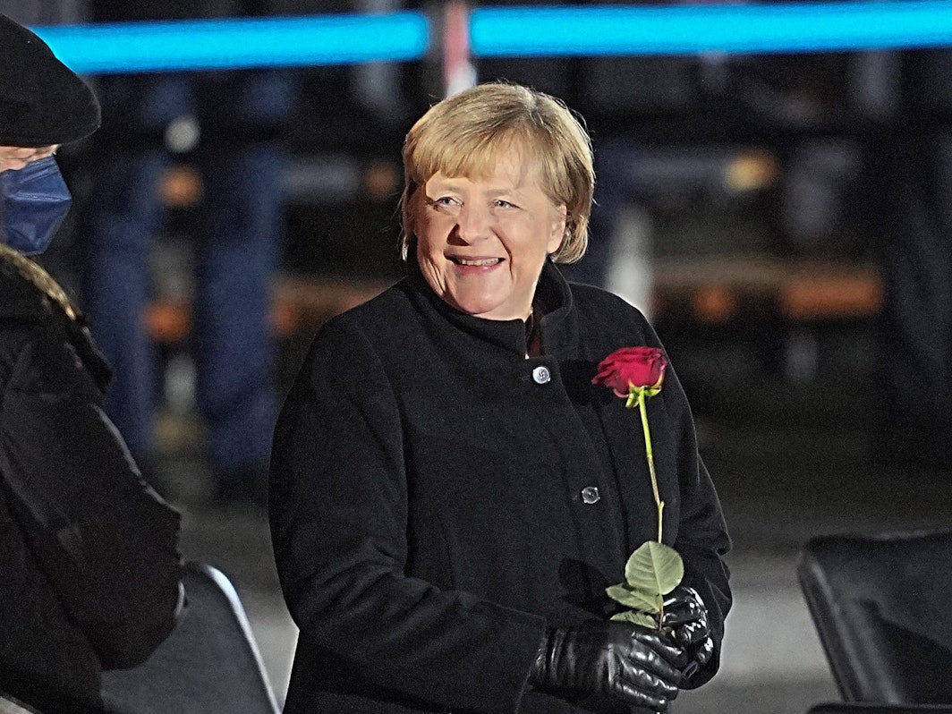Bundeskanzlerin Angela Merkel lacht nach ihrer Verabschiedung durch die Bundeswehr (Foto: 2. Dezember 2021) mit einer Rosen in der Hand neben ihrem Mann, Joachim Sauer.