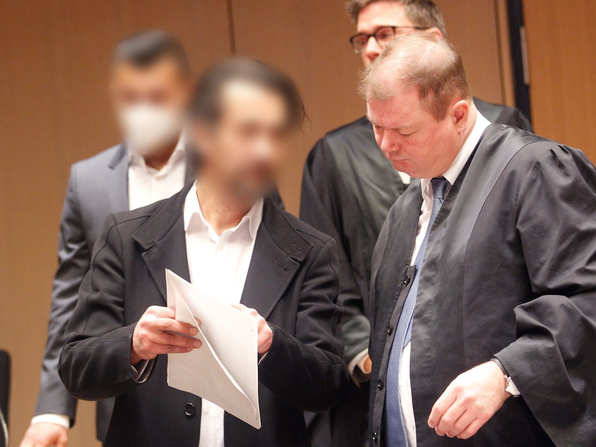Zwei Männer stehen in Bochum vor Gericht, einer zeigt seinem Verteidiger ein Schriftstück.