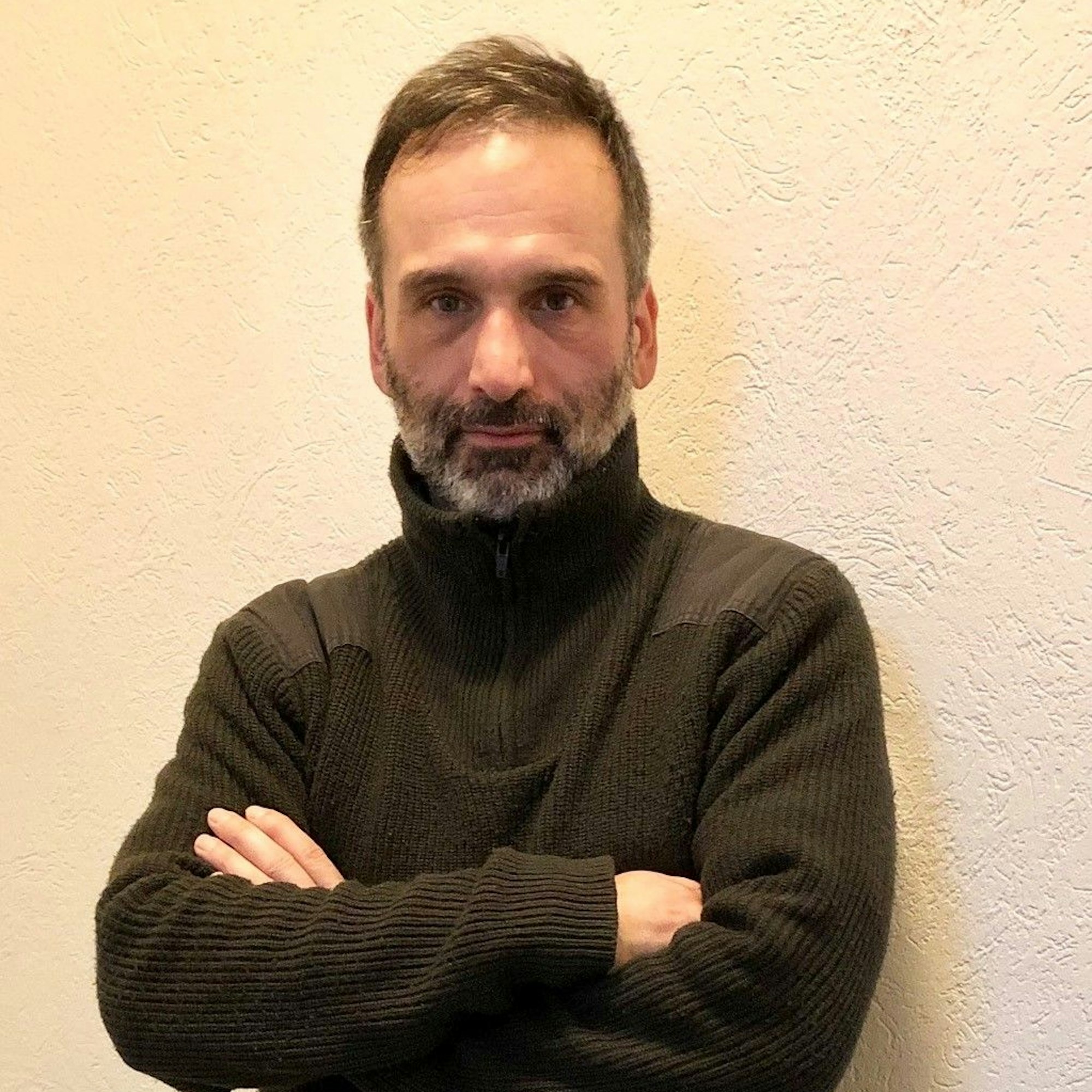 Arthur Nergelian steht mit verschränkten Armen vor einer Wand.