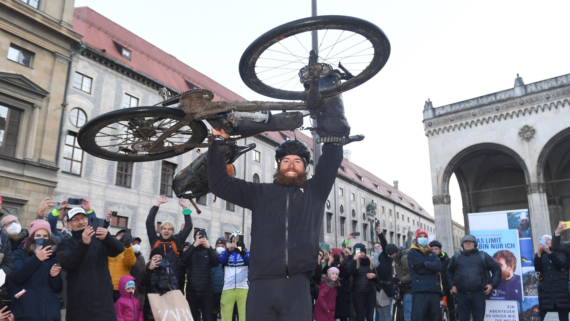 Der deutsche Extremsportler Jonas Deichmann hebt am Odeonsplatz im Ziel seines Triathlon um die Welt sein Fahrrad in die Höhe.