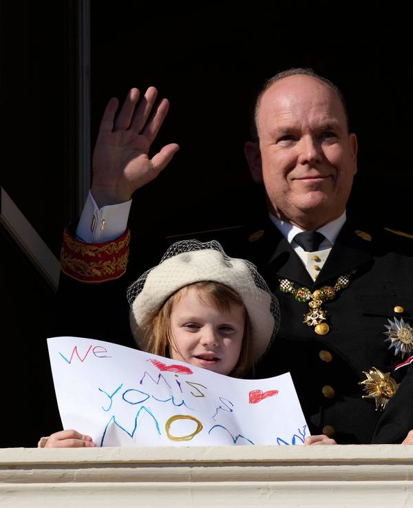 Fürst Albert II. von Monaco (M) winkt während der Feierlichkeiten zum Nationalfeiertag vom Balkon des Palastes von Monaco, während seine Kinder Fürst Jacques und Prinzessin Gabriella von Monaco Bilder mit Botschaften für ihre Mutter Fürstin Charlène in der Hand halten.