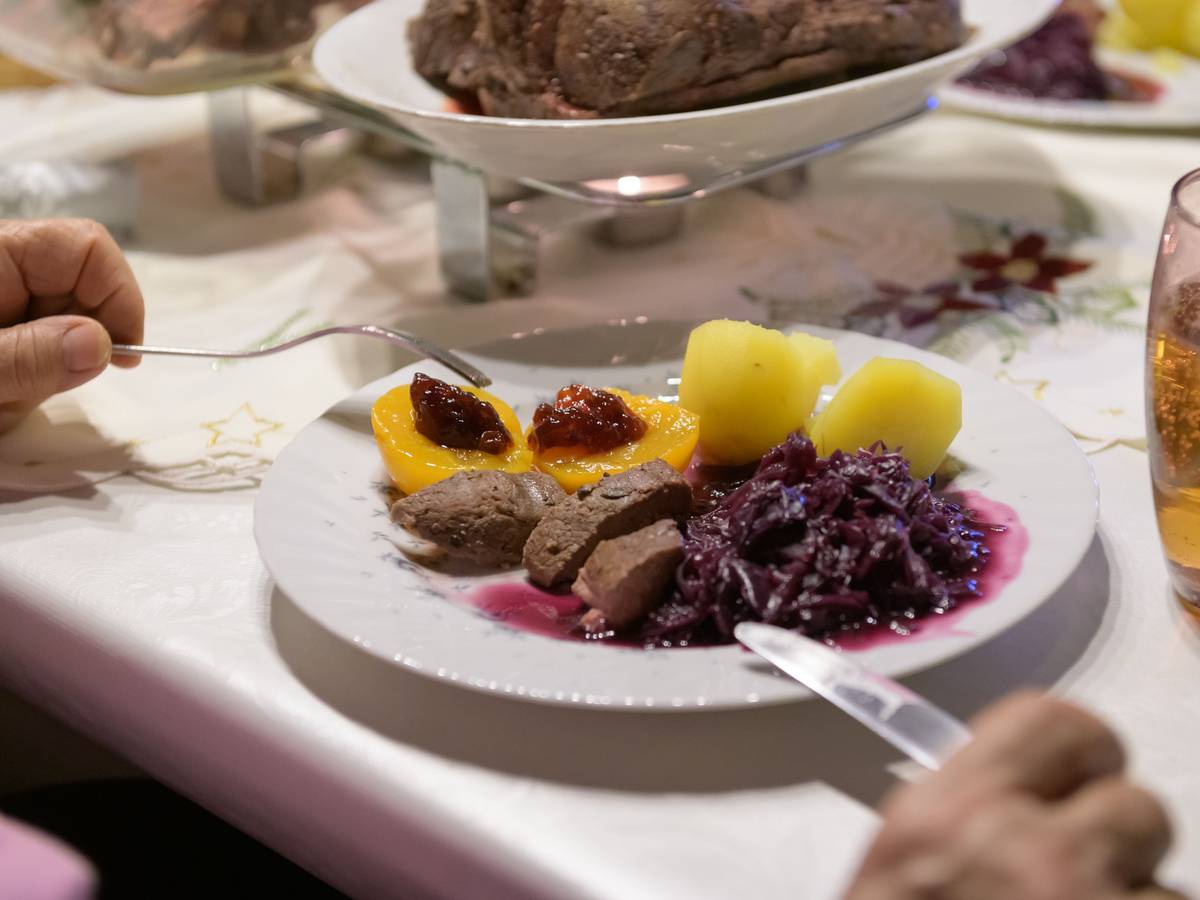 Damhirsch-Rücken mit Kartoffeln und Rotkohl sowie Preiselbeergelee auf Aprikosen liegen verzehrfertig auf einem Teller an Heiligabend.
