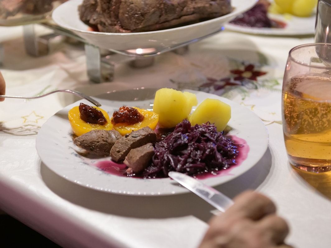 Damhirsch-Rücken mit Kartoffeln und Rotkohl sowie Preiselbeergelee auf Aprikosen liegen verzehrfertig auf einem Teller an Heiligabend.