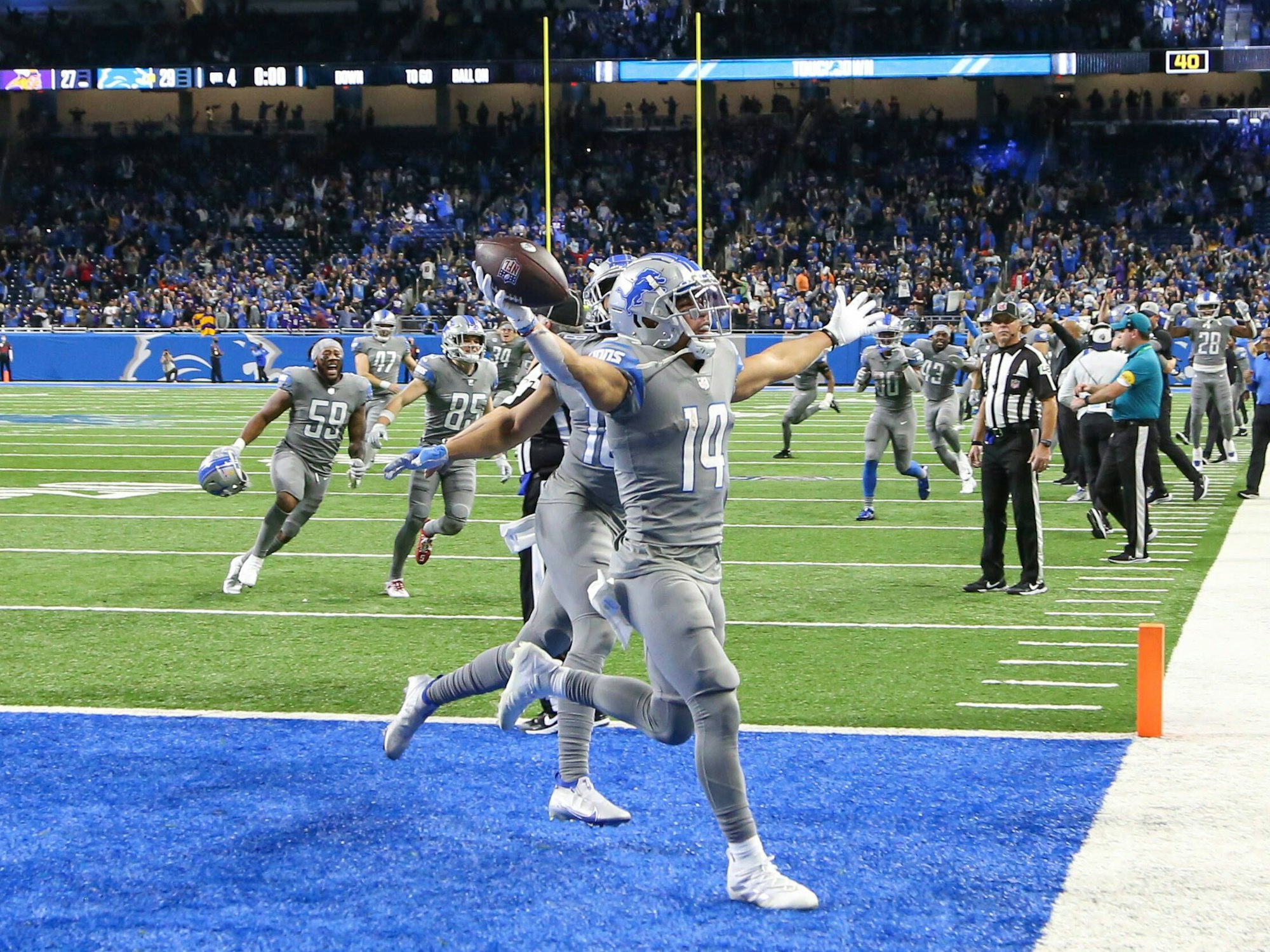 Amon-Ra St. Brown hält den Football in der Hand, breitet dabei die Arme aus. Seine Mitspieler rennen ihm hinterher.