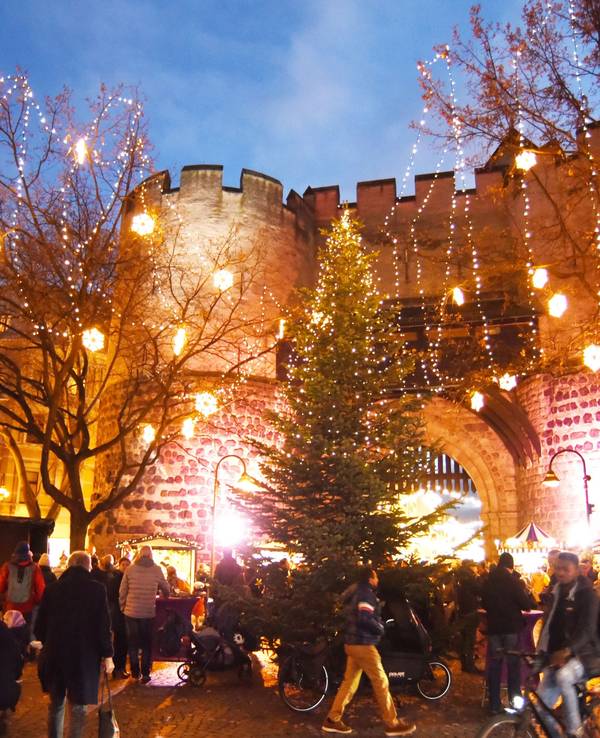 Besucher und Besucherinnen laufen über der Weihnachtsmarkt am Kölner Eigelstein – im Hintergrund die Torburg.