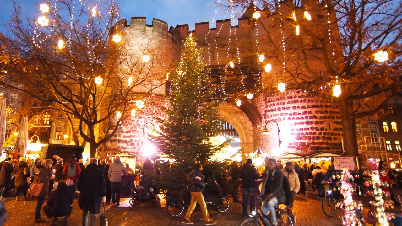 Besucher und Besucherinnen laufen über der Weihnachtsmarkt am Kölner Eigelstein – im Hintergrund die Torburg.