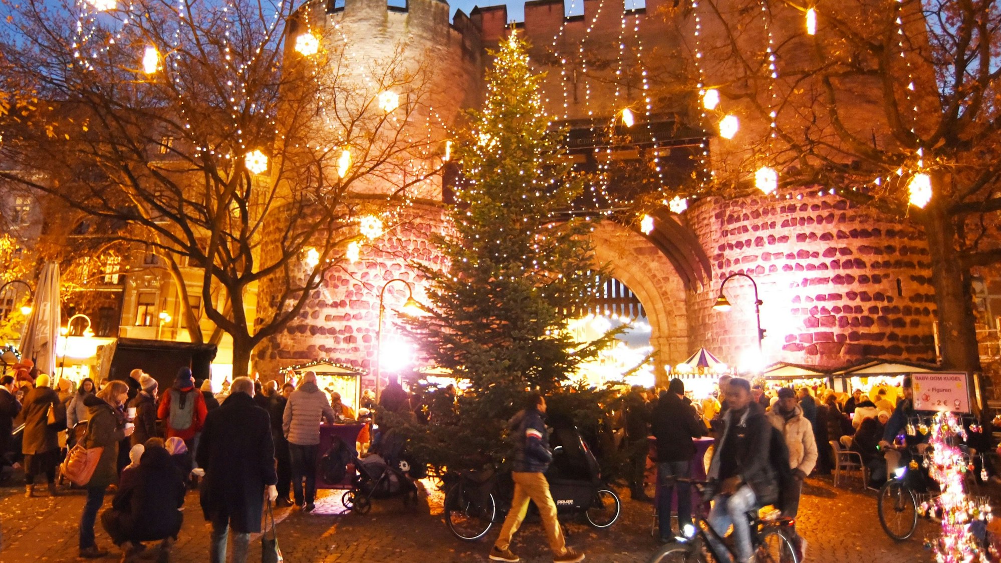 Besucher und Besucherinnen laufen über der Weihnachtsmarkt am Kölner Eigelstein – im Hintergrund die Torburg.