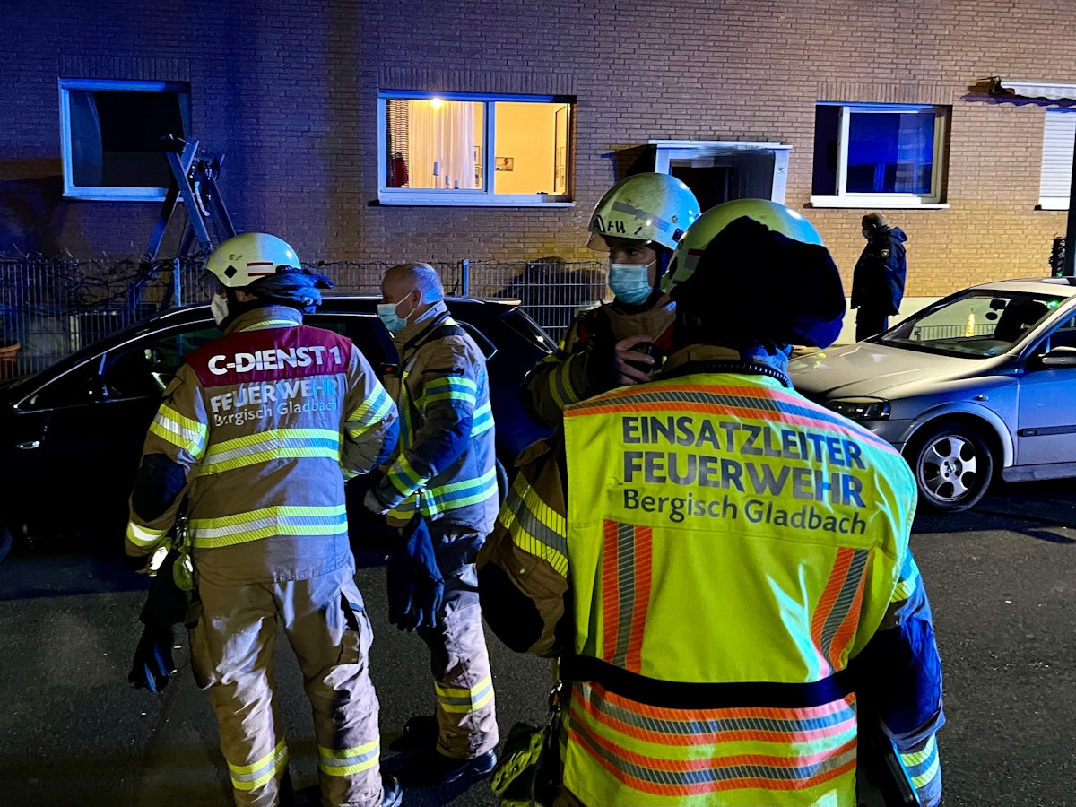 Feuerwehr-Leute stehen auf der Straße vor einem beleuchteten Haus.