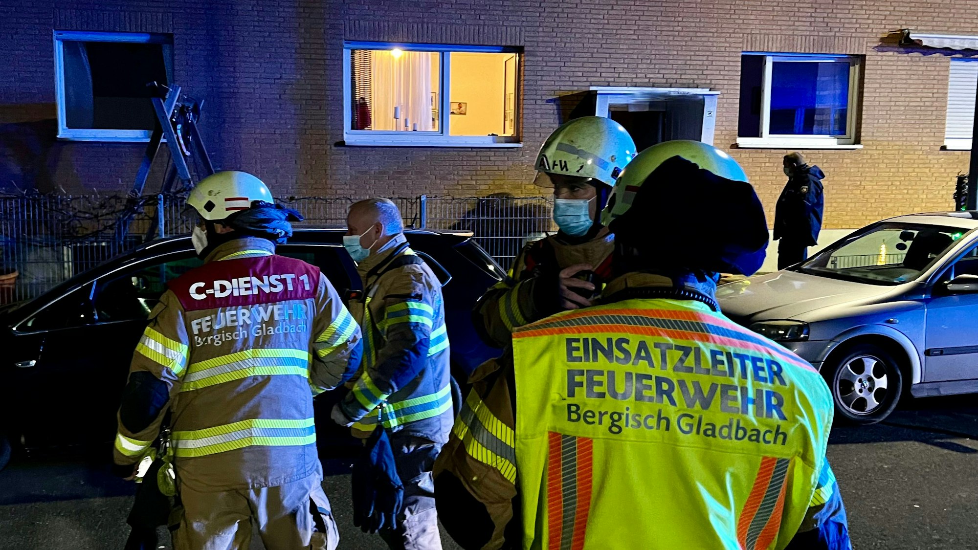 Feuerwehr-Leute stehen auf der Straße vor einem beleuchteten Haus.