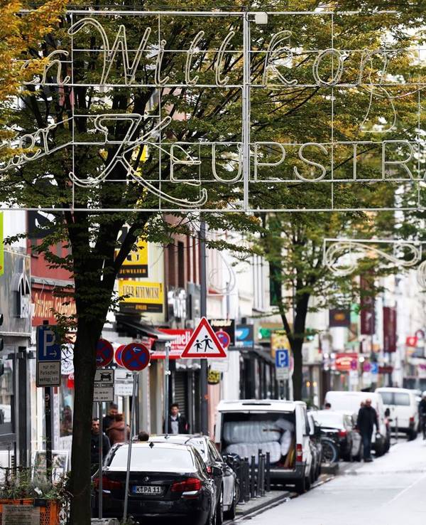 Köln: Die Keupstrasse mit mehreren Geschäften, Fußgängern und Autos.