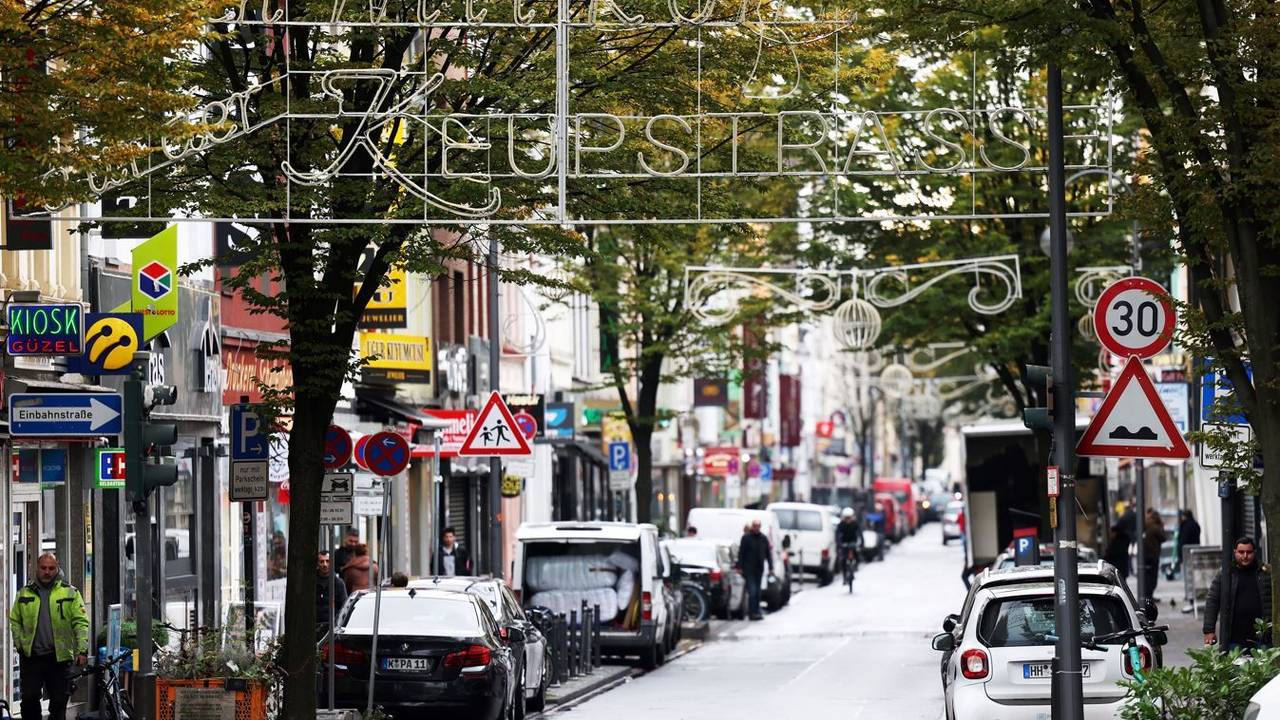 Köln: Die Keupstrasse mit mehreren Geschäften, Fußgängern und Autos.