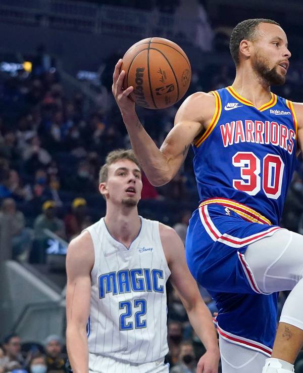 Stephen Curry springt hoch zum Korb. Franz Wagner steht wie angewurzelt dahinter. Auch Mo Bamba ha keinen Zugriff.