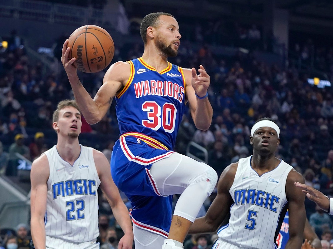 Stephen Curry springt hoch zum Korb. Franz Wagner steht wie angewurzelt dahinter. Auch Mo Bamba ha keinen Zugriff.