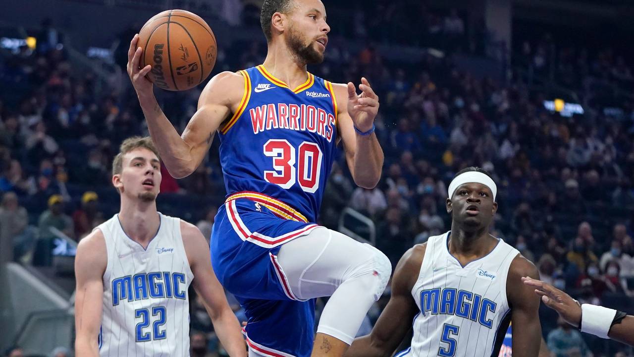 Stephen Curry springt hoch zum Korb. Franz Wagner steht wie angewurzelt dahinter. Auch Mo Bamba ha keinen Zugriff.