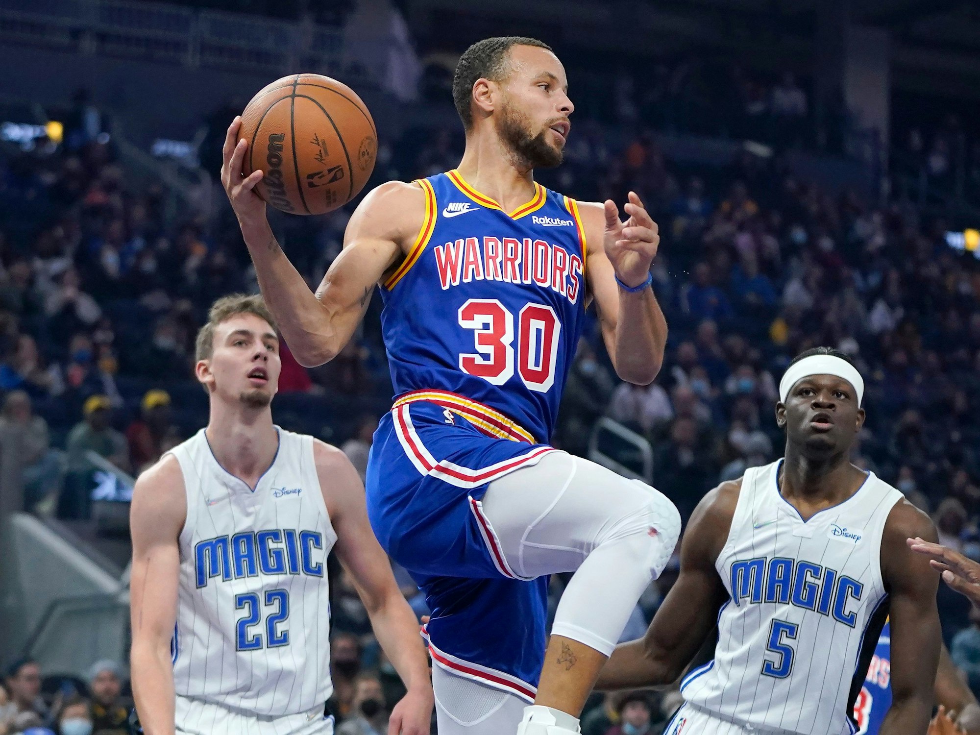 Stephen Curry springt hoch zum Korb. Franz Wagner steht wie angewurzelt dahinter. Auch Mo Bamba ha keinen Zugriff.