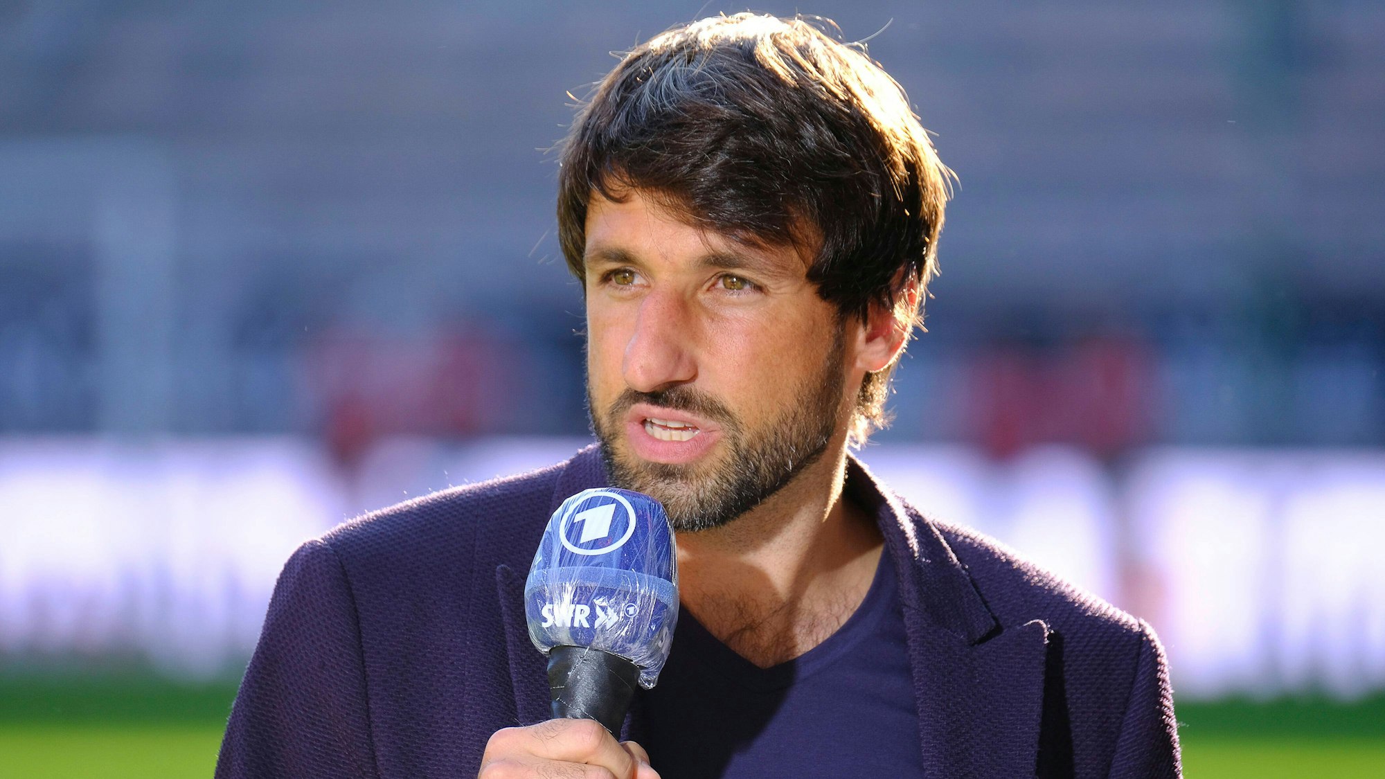 Thomas Broich hält ein ARD-Mirko in der Hand und steht im Stadion des 1. FC Kaiserslautern.