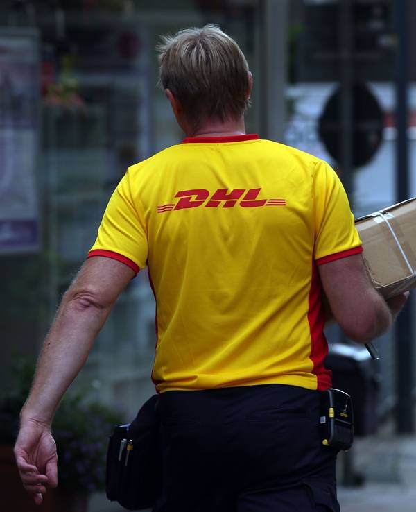 Ein Paketzustellerder von Deutsche Post DHL liefert ein Paket aus.