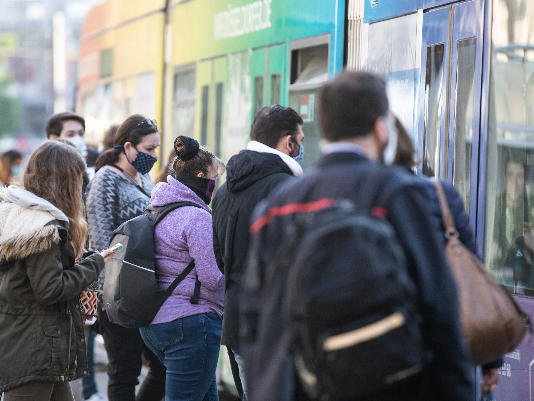 Zahlreiche Pendler warten am Morgen mit verschiedenen Gesichtsbedeckungen vor einer Straßenbahn in Düsseldorf.
