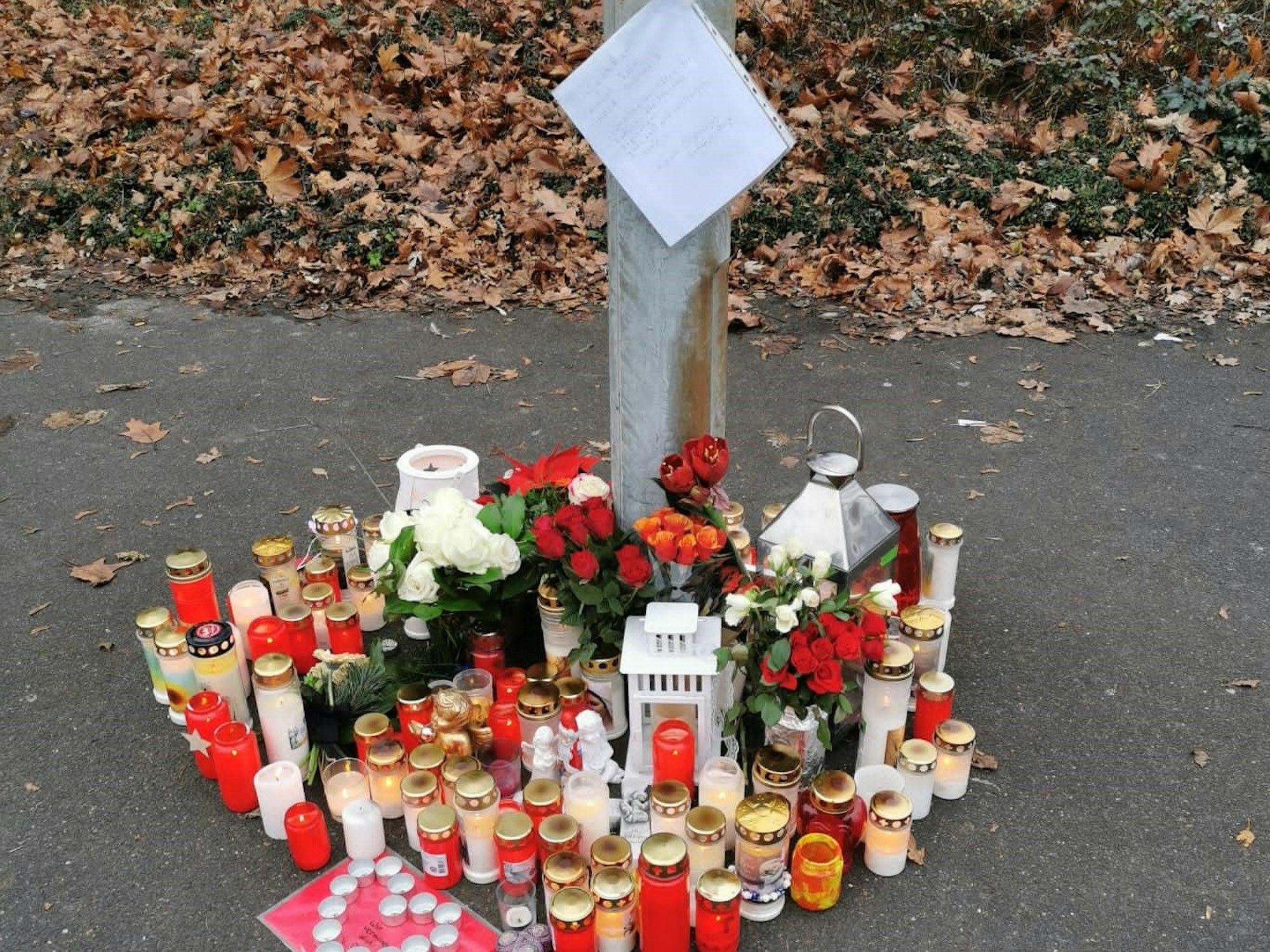 Die Trauerstelle mit vielen Kerzen und Blumen auf dem Asphalt.