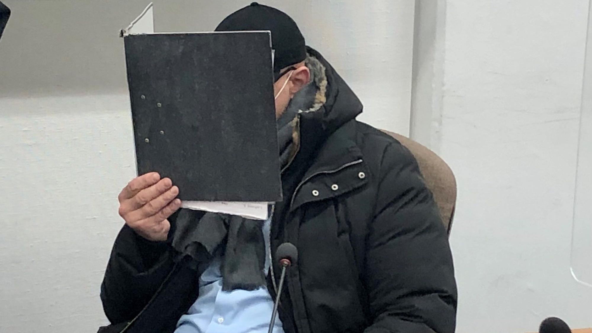 Der angeklagte Security-Boss hält sich beim Prozessauftakt einen Aktenordner vor das Gesicht.