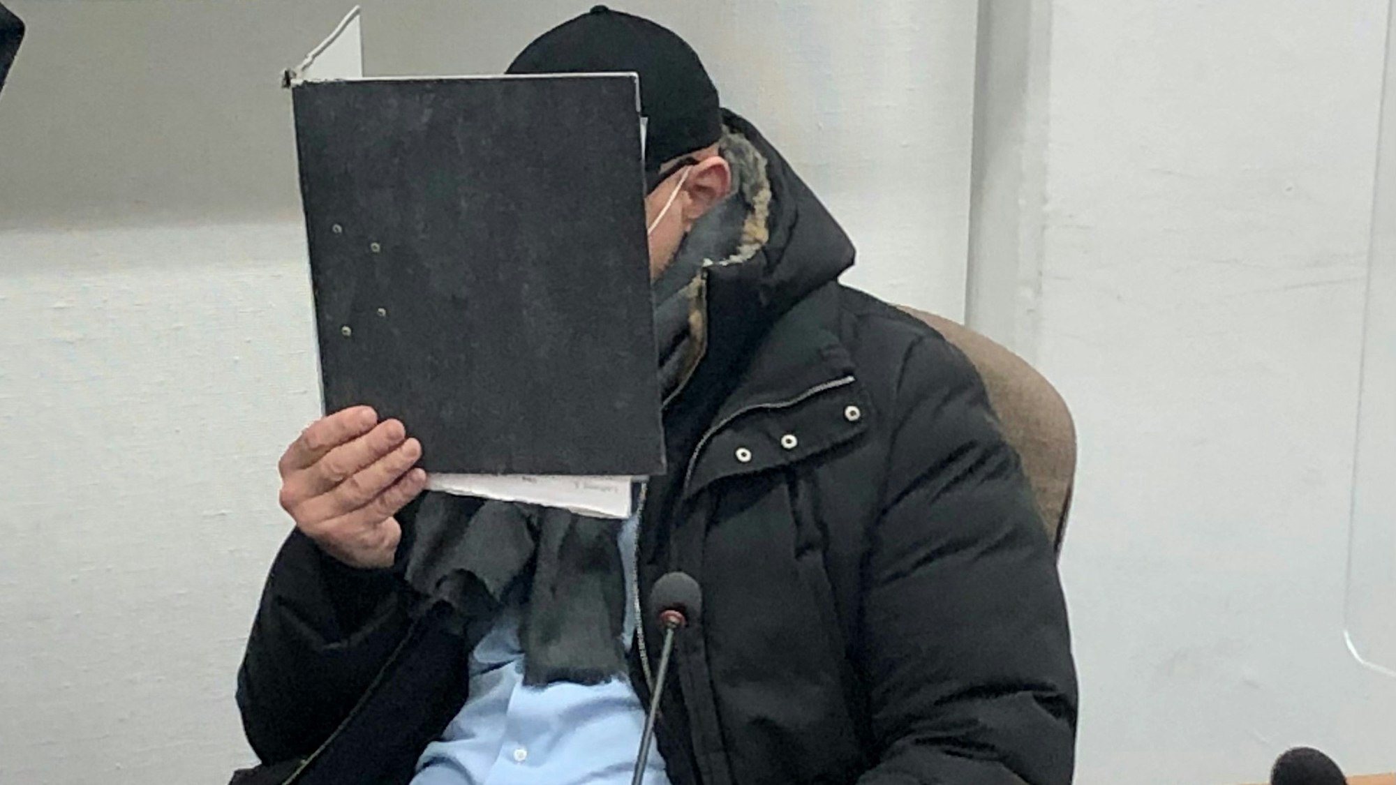 Der angeklagte Security-Boss hält sich beim Prozessauftakt einen Aktenordner vor das Gesicht.