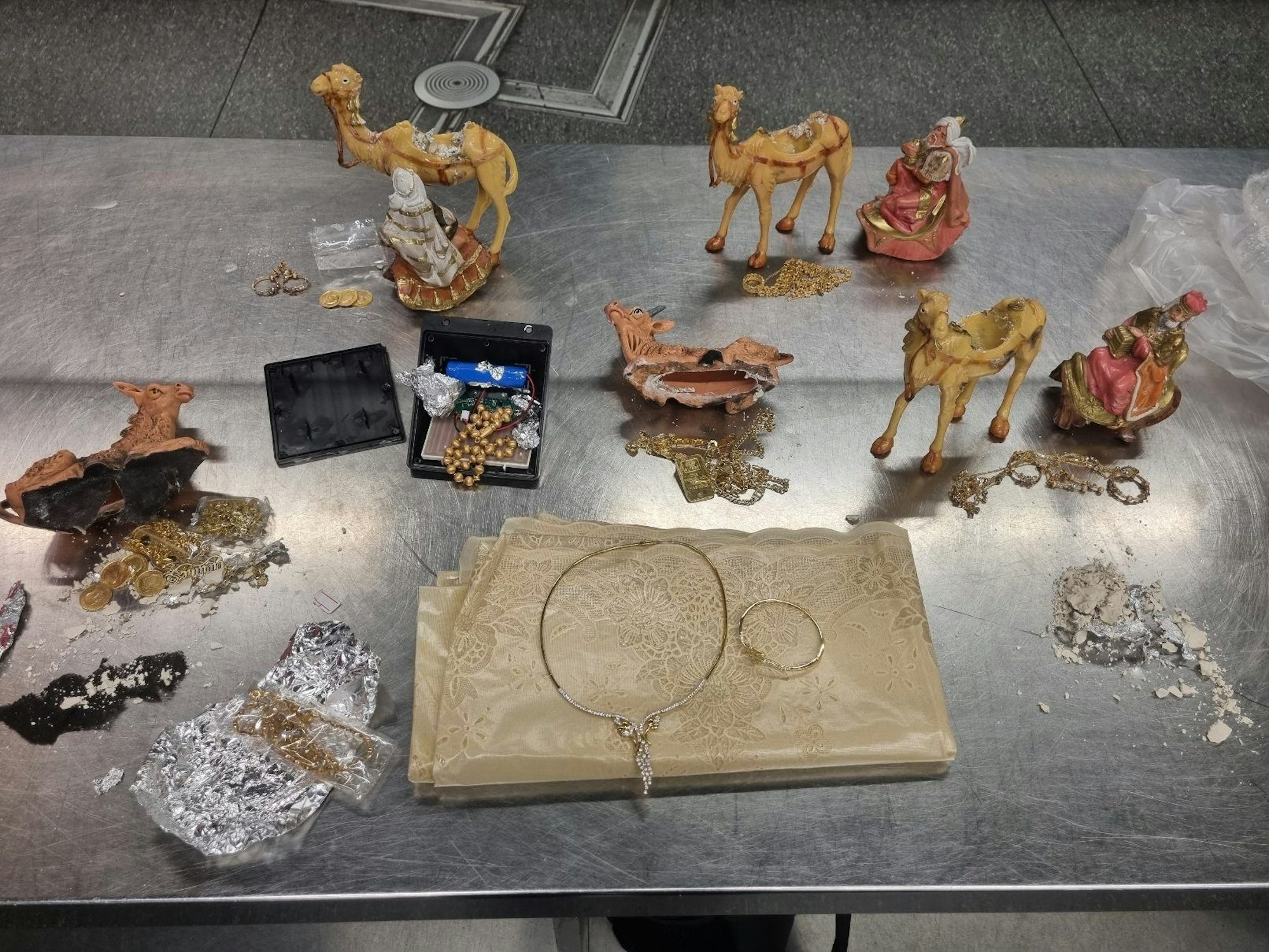 Auf einem Tablett stehen aufgebrochene Krippenfiguren, Goldschmuck und Goldmünzen.