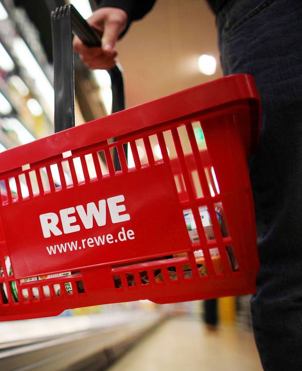 Ein Kunde geht in einem Rewe-Supermarkt mit einem Einkaufskorb am Kühlregal entlang.