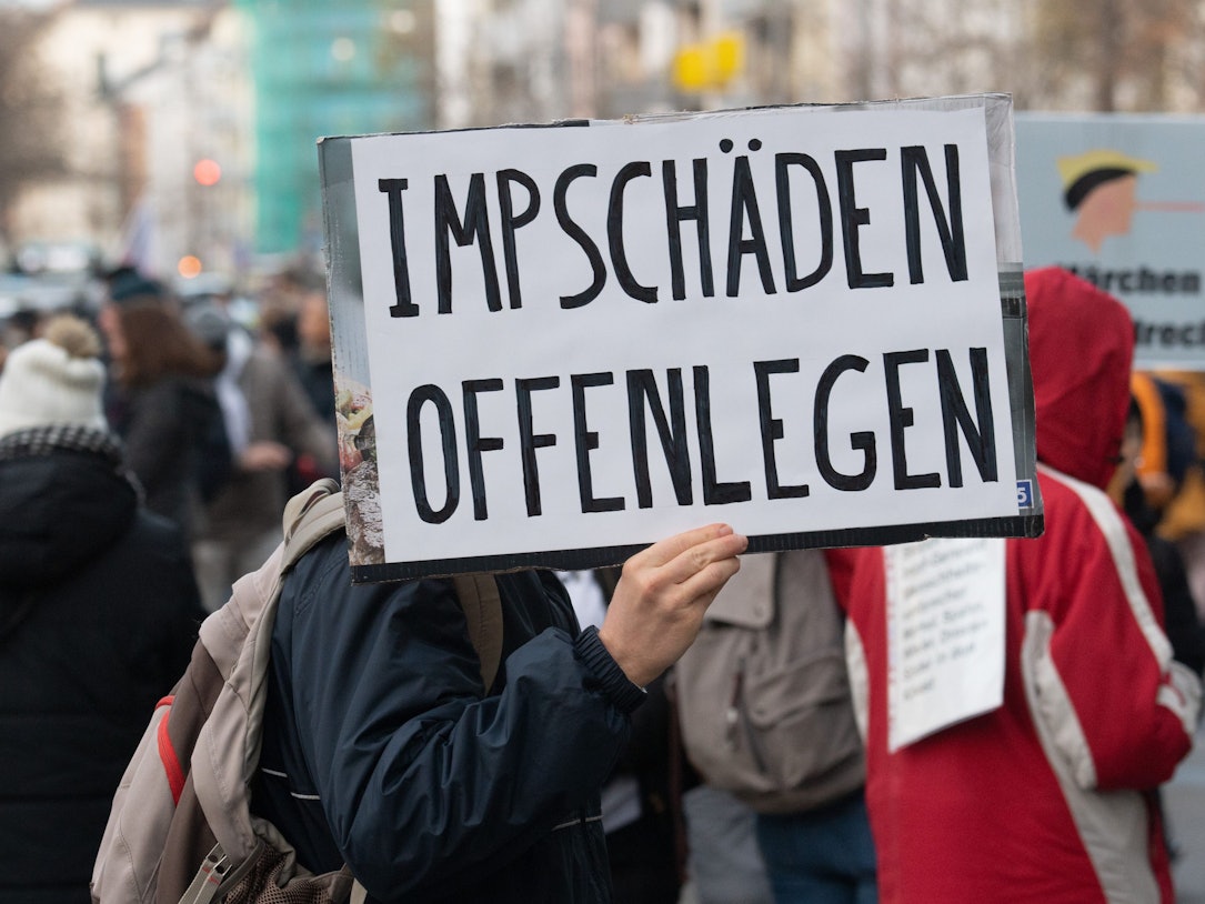Ein Teilnehmer einer Demonstration hält ein Schild mit der Aufschrift „Impfschäden offenlegen“ in der Hand.