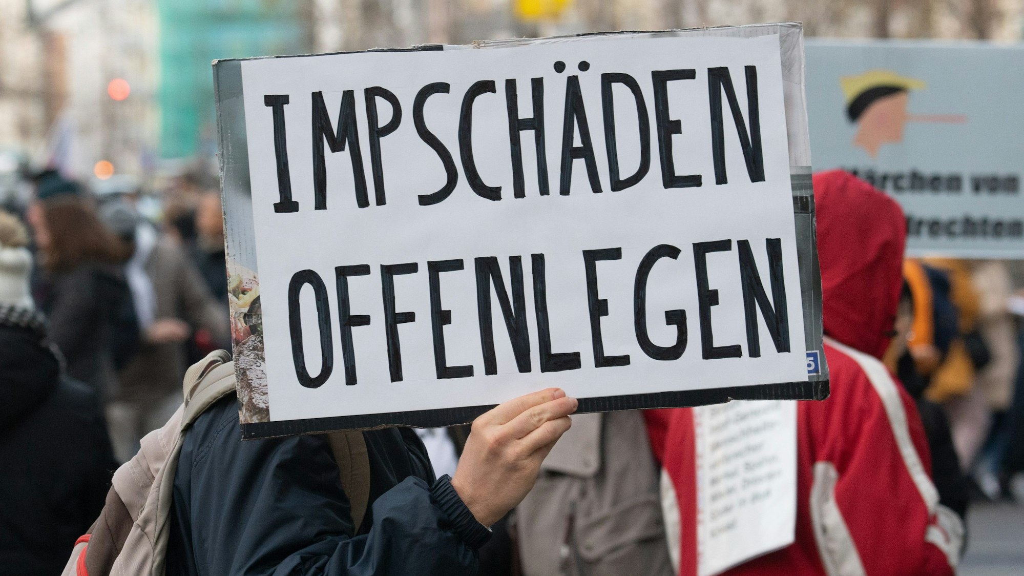 Ein Teilnehmer einer Demonstration hält ein Schild mit der Aufschrift „Impfschäden offenlegen“ in der Hand.