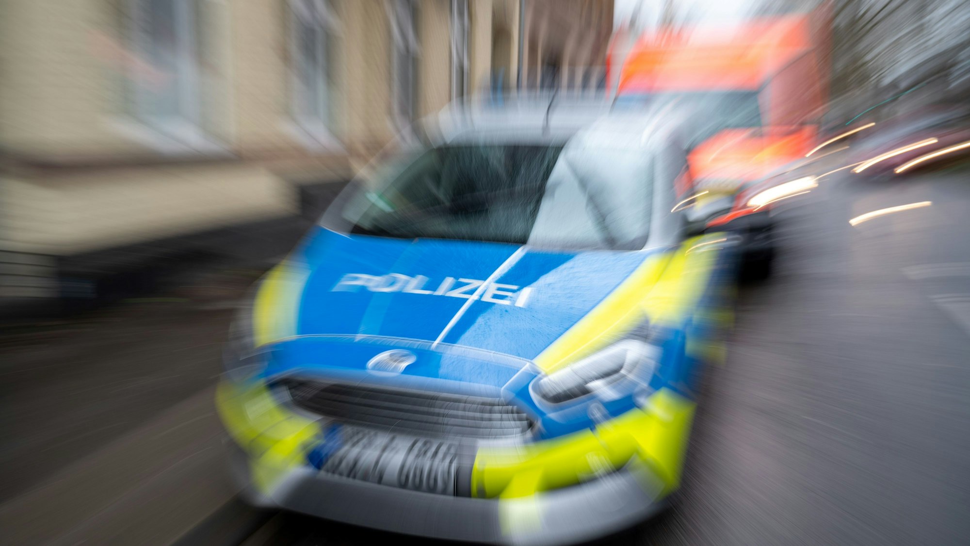 Ein fahrendes Polizeiauto ist zentral auf dem Bild zu sehen, dicht gefolgt von einem Rettungswagen.