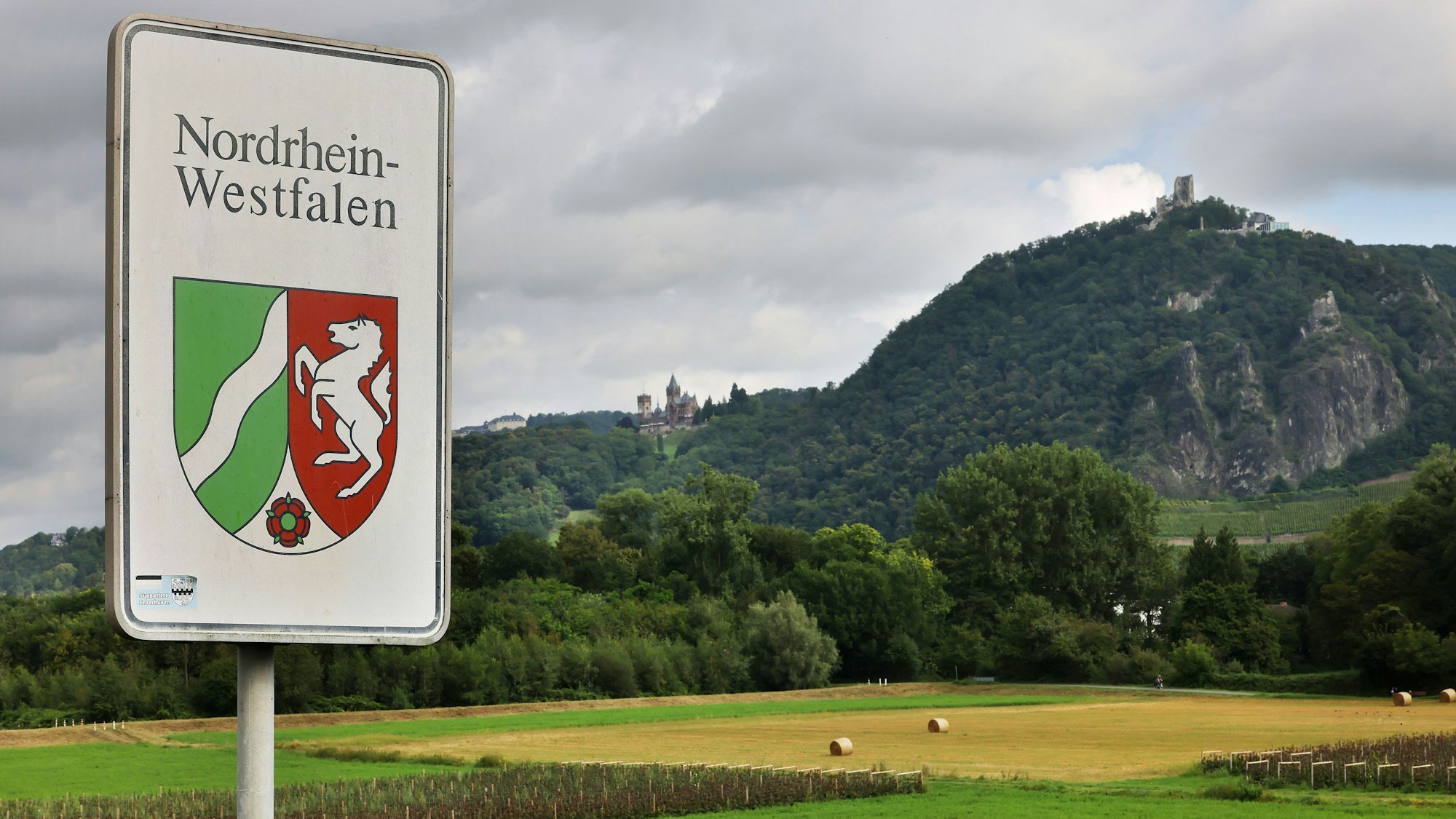 Ein Strassenschild mit dem Landeswappen steht an der Grenze zwischen Nordrhein-Westfalen und Rheinland-Pfalz vor der Kulisse des Drachenfelses.
