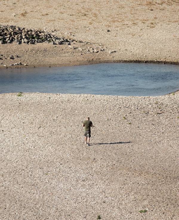 Ein Mann geht am 15. Oktober 2018 bei Niedrigwasser am Rhein entlang. Auch in diesem Jahr hatte der Rhein wieder extremes Niedrigwasser. Ereignisse wie dieses häufen sich in der Klimakrise.