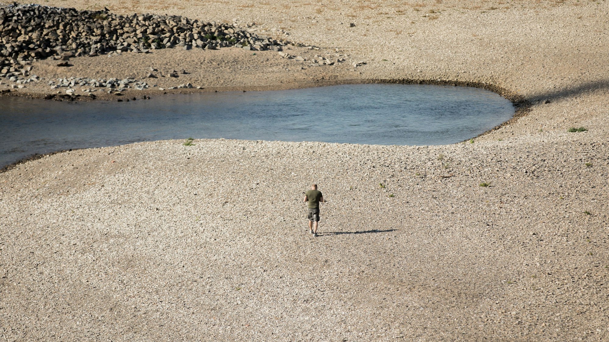 Ein Mann geht am 15. Oktober 2018 bei Niedrigwasser am Rhein entlang. Auch in diesem Jahr hatte der Rhein wieder extremes Niedrigwasser. Ereignisse wie dieses häufen sich in der Klimakrise.