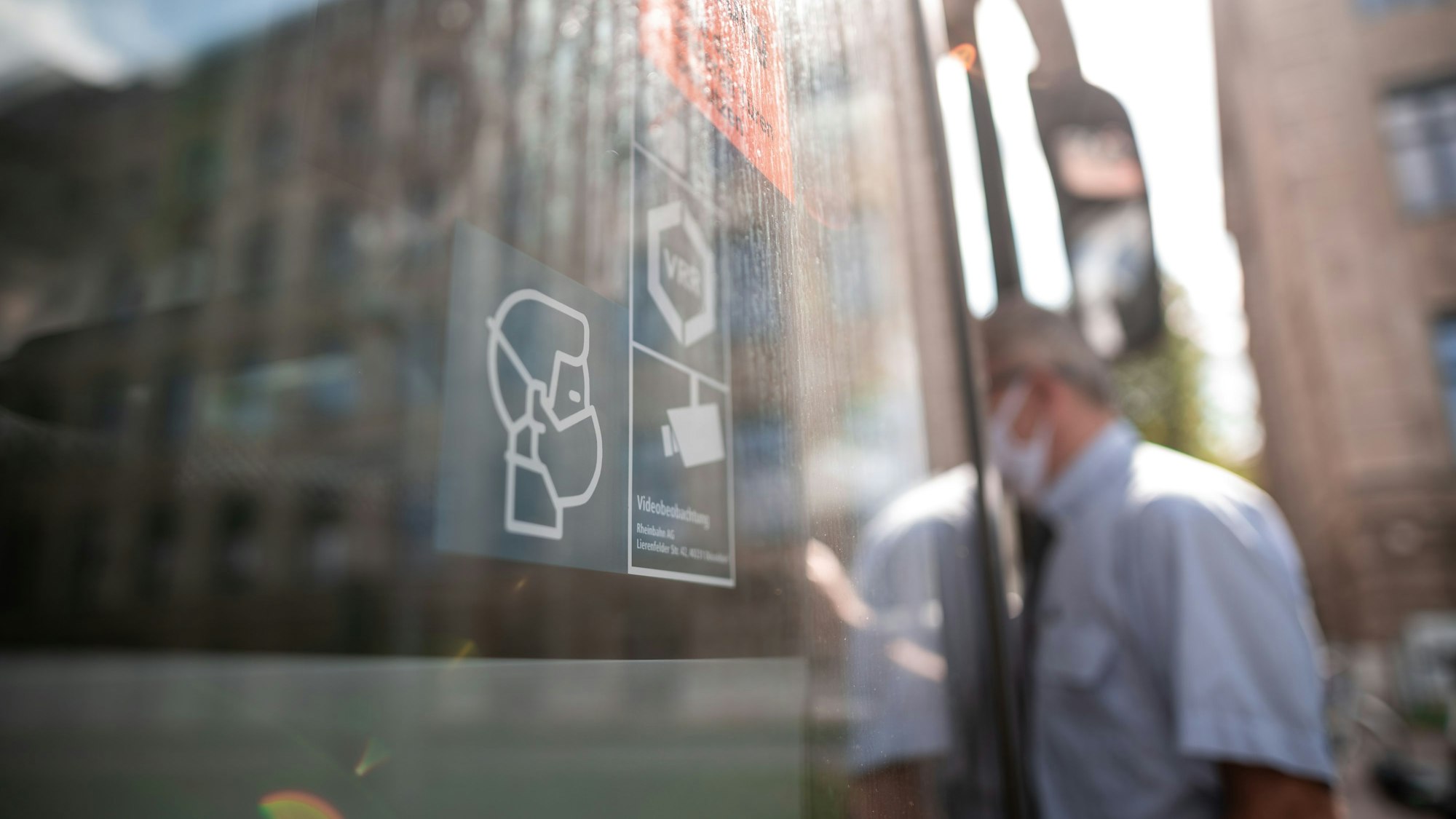 Ein Mann steigt mit Maske in einen Bus während im Vordergrund ein Symbol die Maskenpflicht anzeigt.