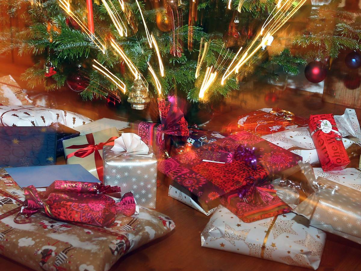 Verpackte Weihnachtsgeschenke liegen unter einem Christbaum.
