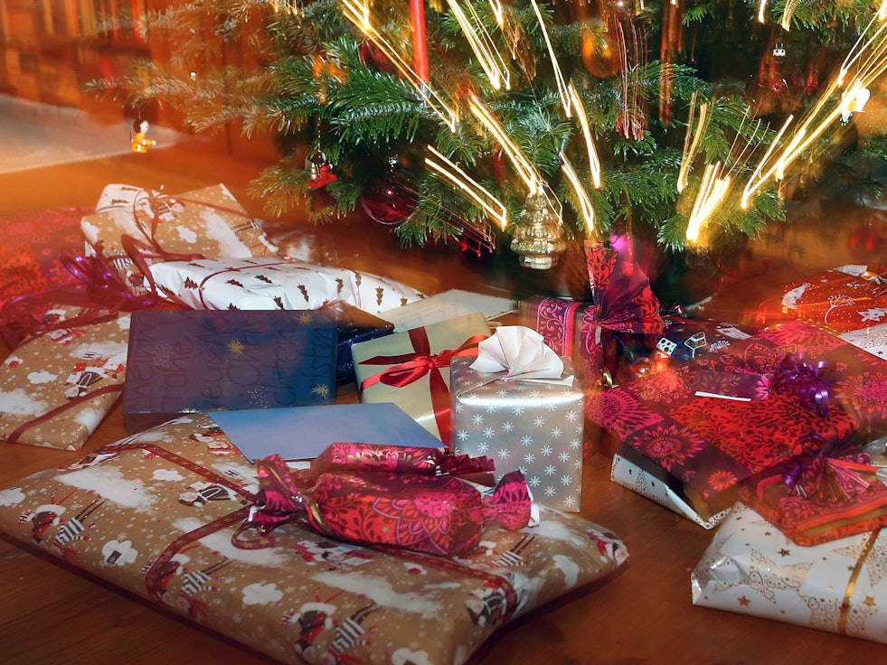Verpackte Weihnachtsgeschenke liegen unter einem Christbaum.