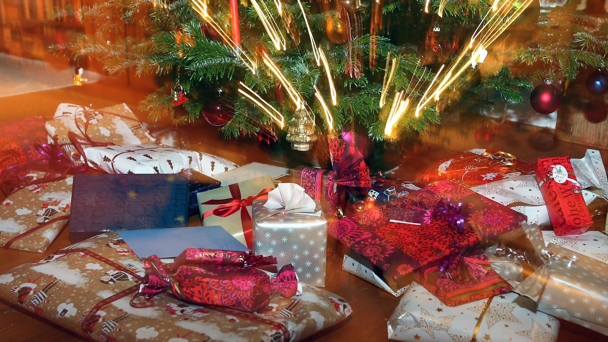 Verpackte Weihnachtsgeschenke liegen unter einem Christbaum.