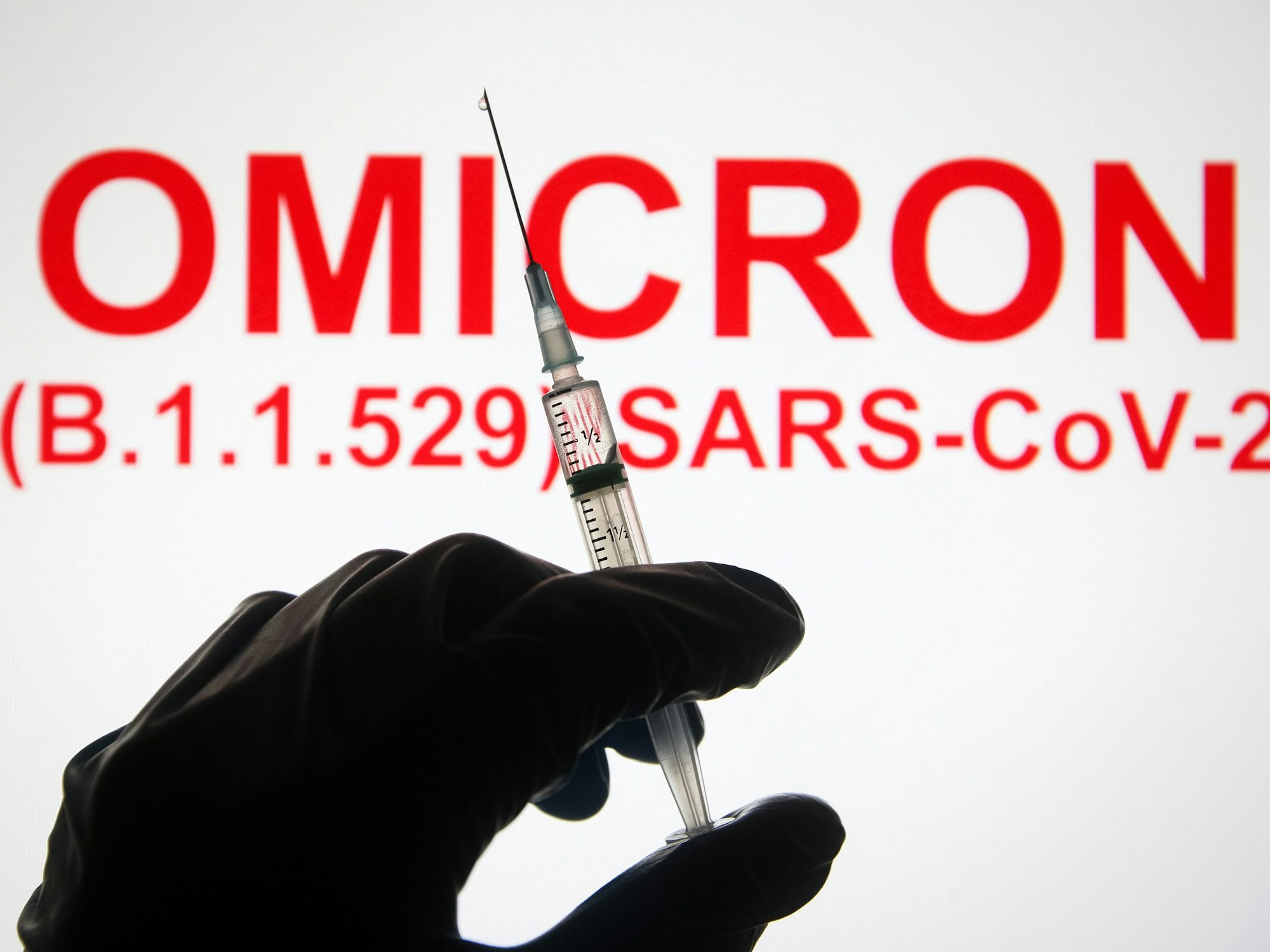Eine Hand hält vor der Aufschrift „Omicron (B.1.1.529): SARS-CoV-2“ eine Spritze hoch.